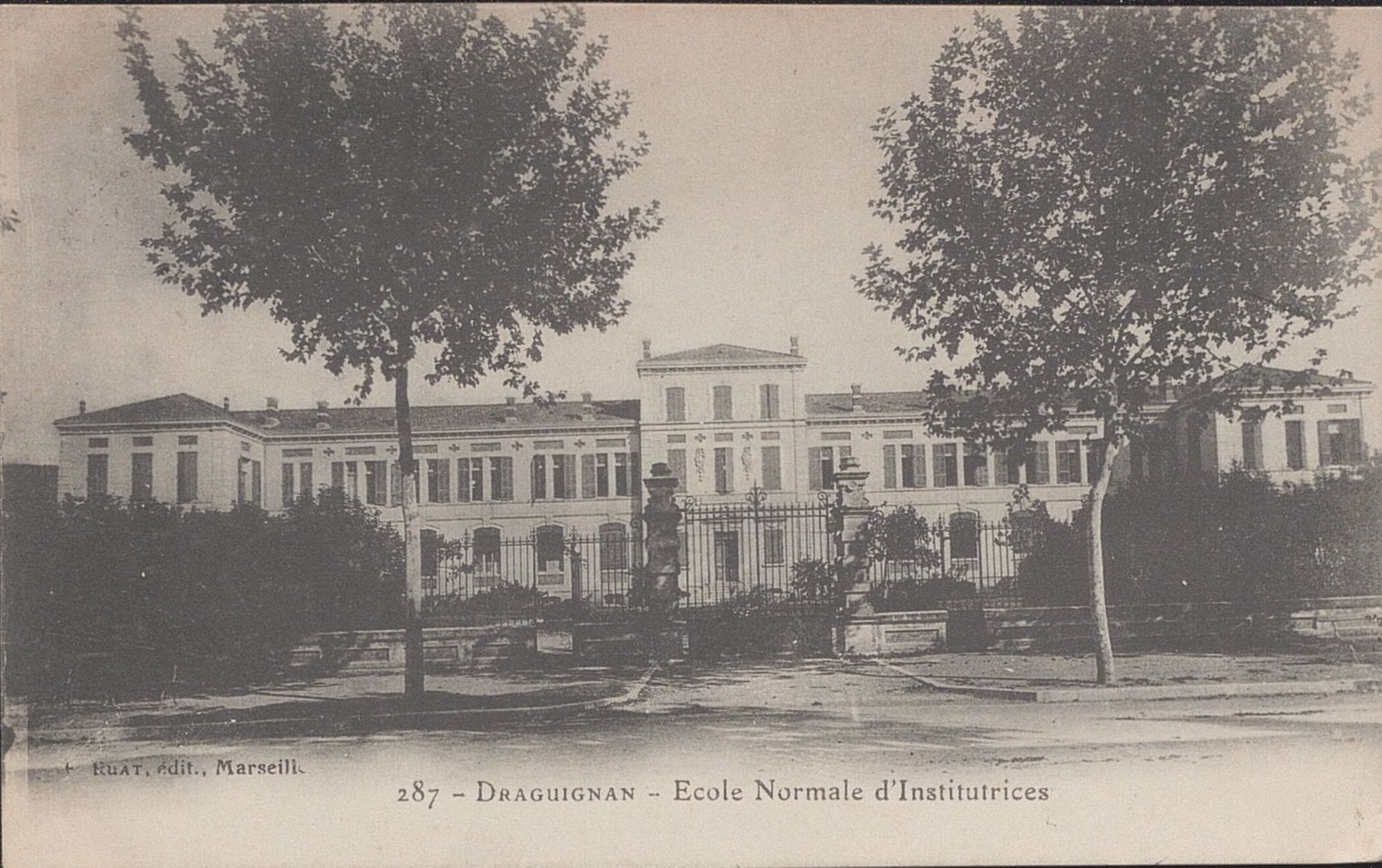 Sur la photographie en noir et blanc de cette carte postale, nous distinguons les différences entre le projet réalisé et l'avant projet, malgré la végétation et le portail qui empêchent de voir correctement le rez-de-chaussée. La partie centrale n'a pas de girouette et les deux avancées sur les côté comportent autant qu'étages que le bâtiment principal.