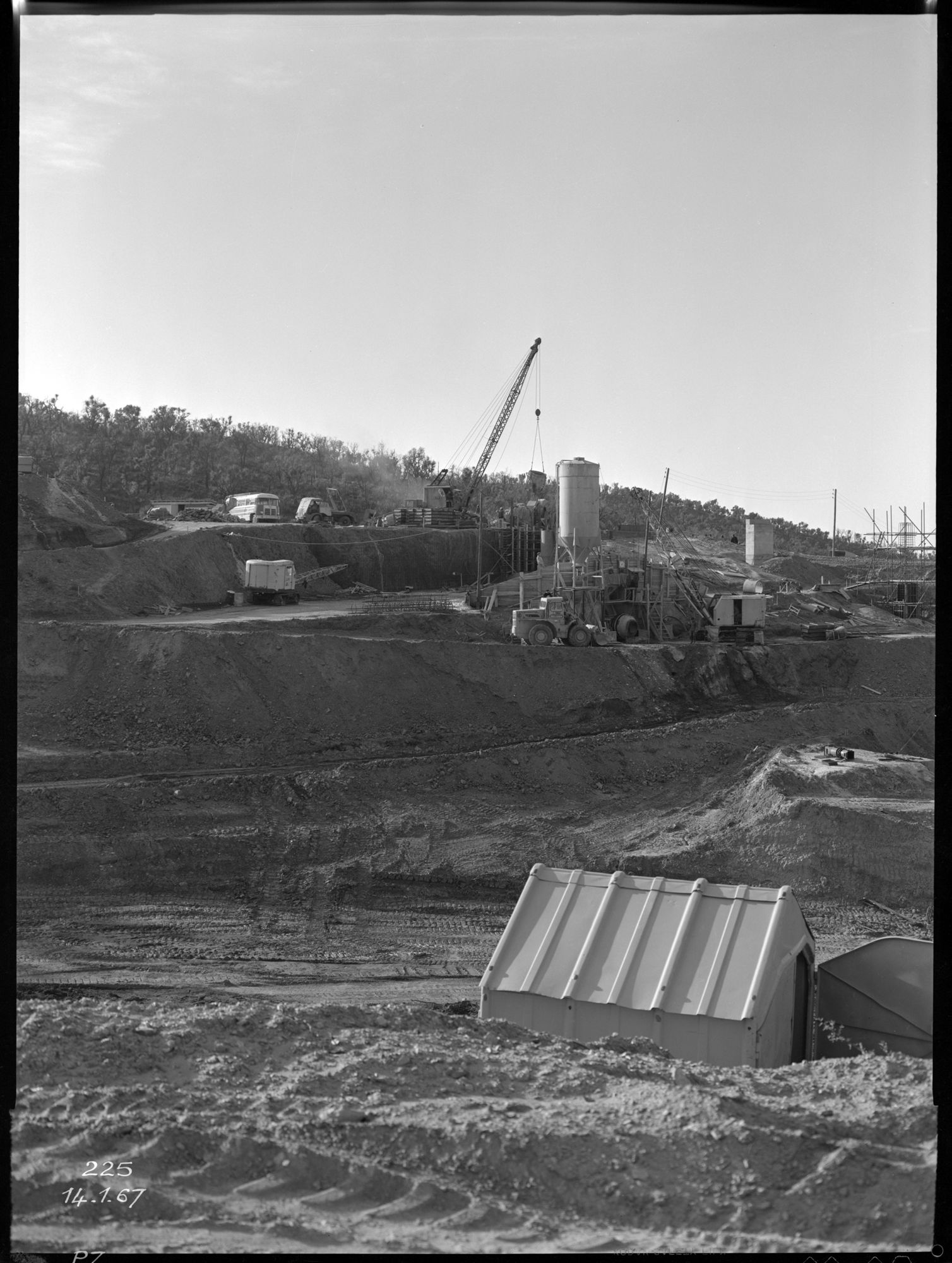 Maison de chantier en tôle au premier plan, chantier, bétonneuse, camions, échafaudage