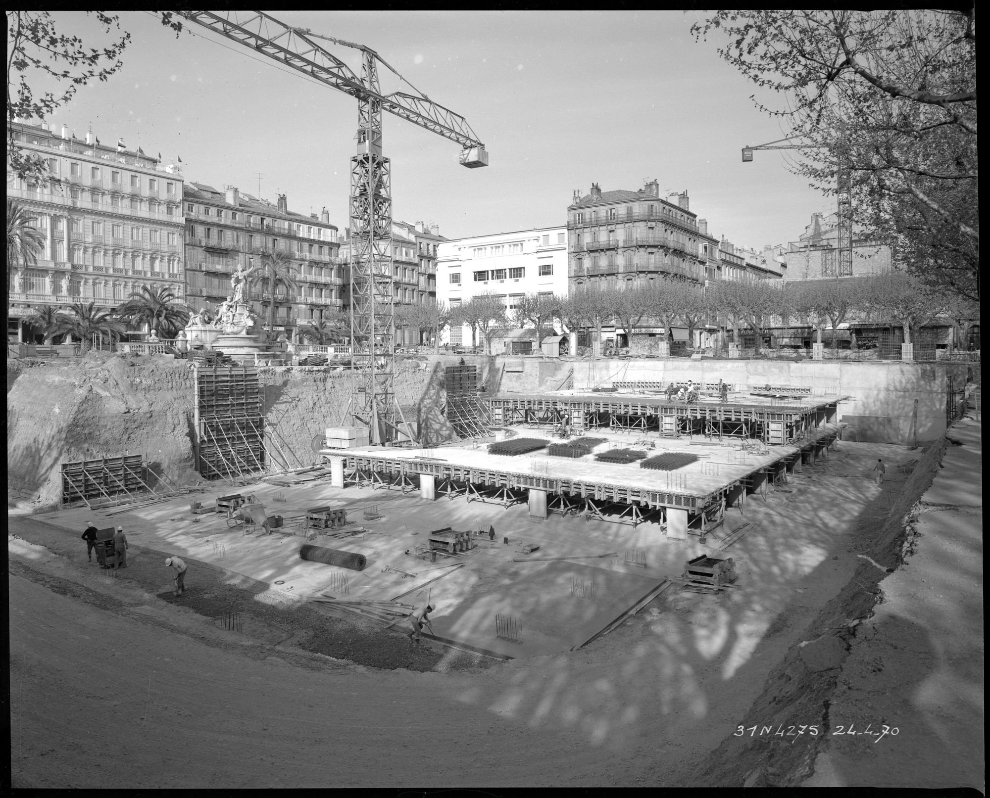 Parking souterrain en construction : 2ème niveaux en sous-sol, grues, ouvriers, immeubles, fontaine